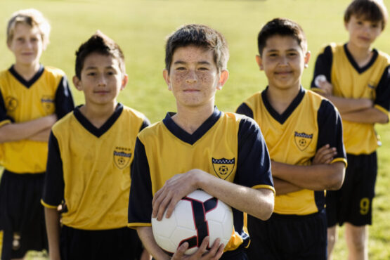 A group of boys in team football shirts, one holding a soccer ball.